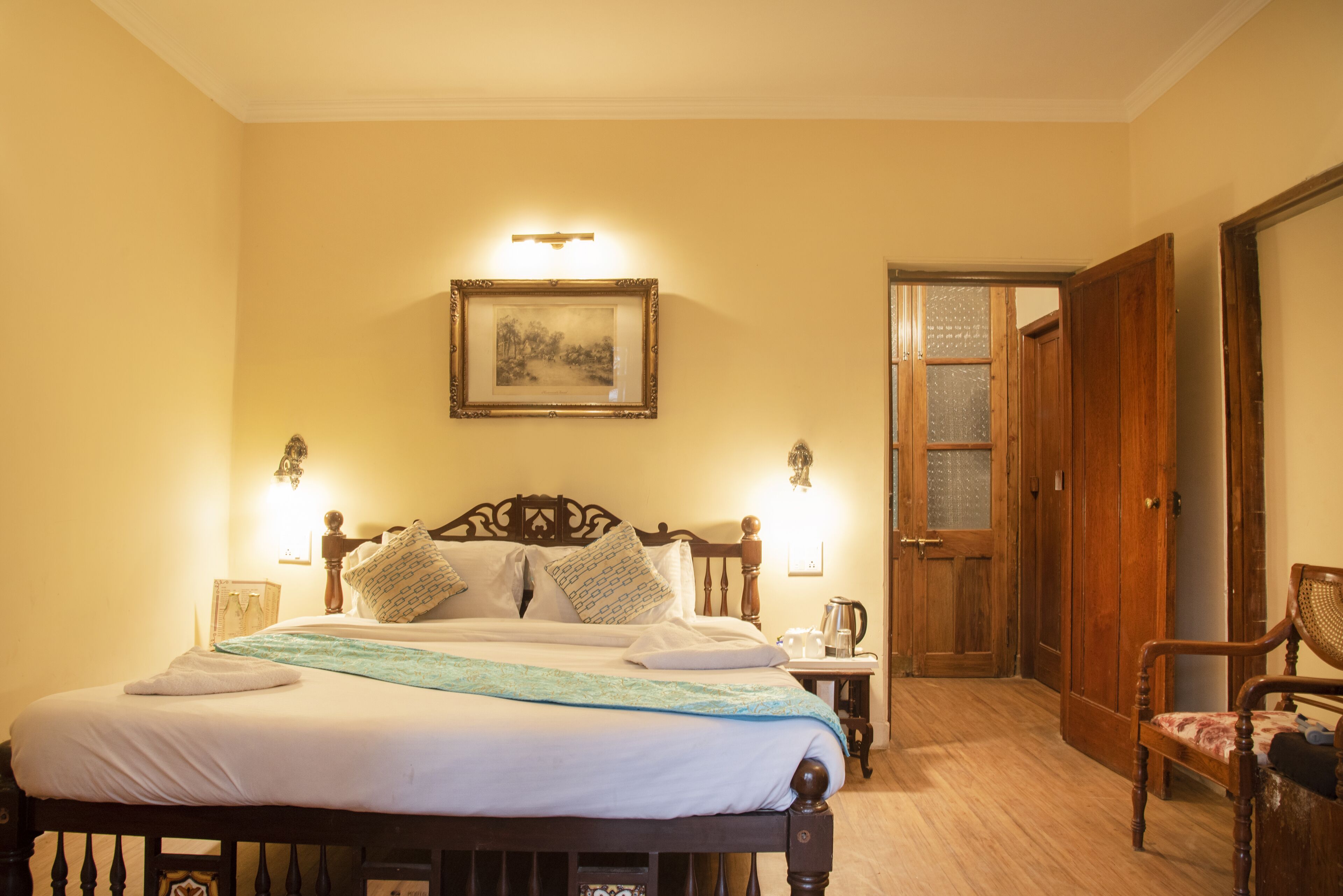 Una cama bien hecha con cabecera de madera, una mesita de noche con lámpara y un cuadro enmarcado en la pared.