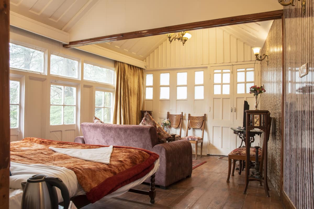 A spacious bedroom with a large bed, a sitting area with a chair and table, and multiple windows providing natural light.