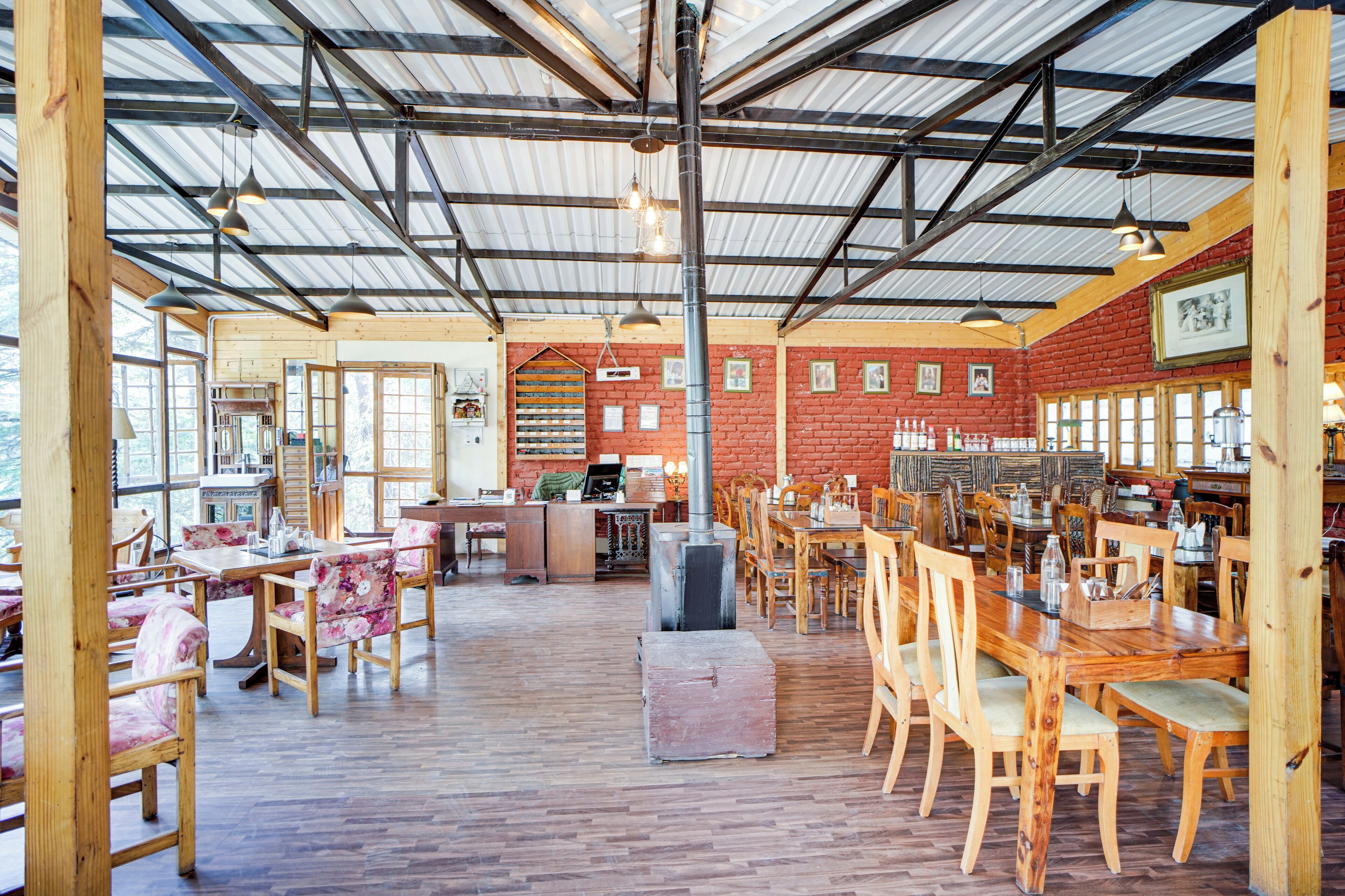 A spacious dining area with wooden tables and chairs, a brick wall, and a high ceiling with metal beams.