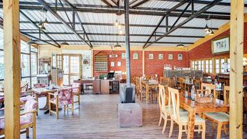 A spacious dining area with wooden tables and chairs, a brick wall, and a high ceiling with metal beams.