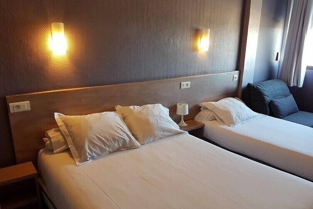 Ein Hotelzimmer mit zwei Betten, jeweils mit weißen Bettwäsche und Kissen, einem Holz-Kopfteil und Wandleuchten.