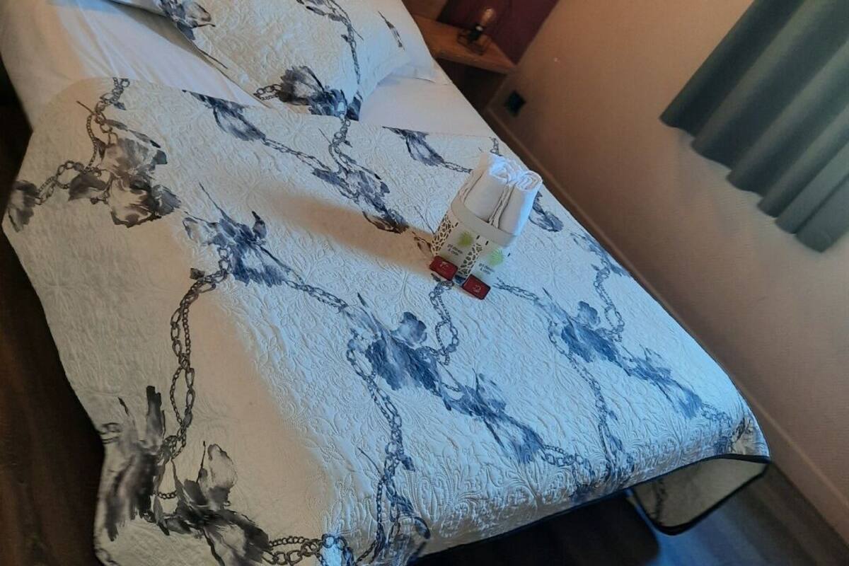 Ein Bett mit blumigem Überwurf, ein Nachttisch mit Lampe und ein Fenster mit Jalousien.