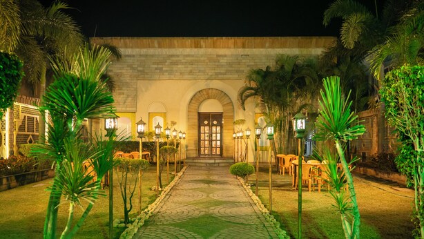 Un cortile con un percorso lastricato che conduce all'ingresso di un edificio, circondato da palme e posti a sedere all'aperto.