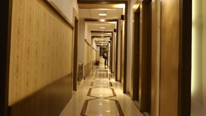 Un corridoio d'albergo con pavimento lucido, pannelli in legno sulle pareti e una serie di porte.