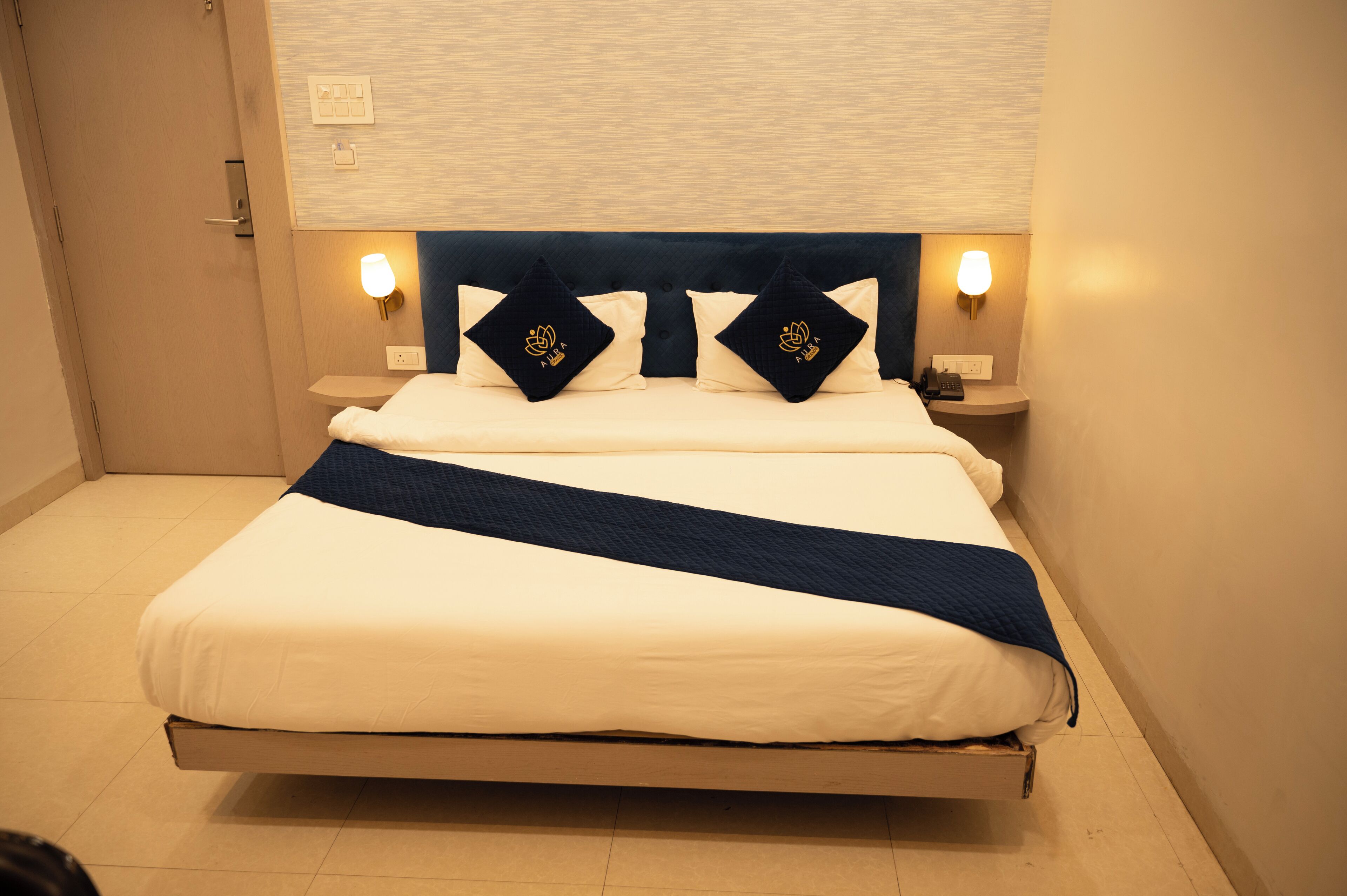 A neatly made bed with a dark headboard, two bedside lamps, and a bedside table with a phone.