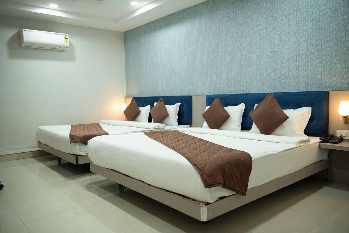Una camera d'albergo con due letti, una testiera blu, biancheria da letto bianca, cuscini decorativi marroni, una lampada da comodino e un condizionatore d'aria.