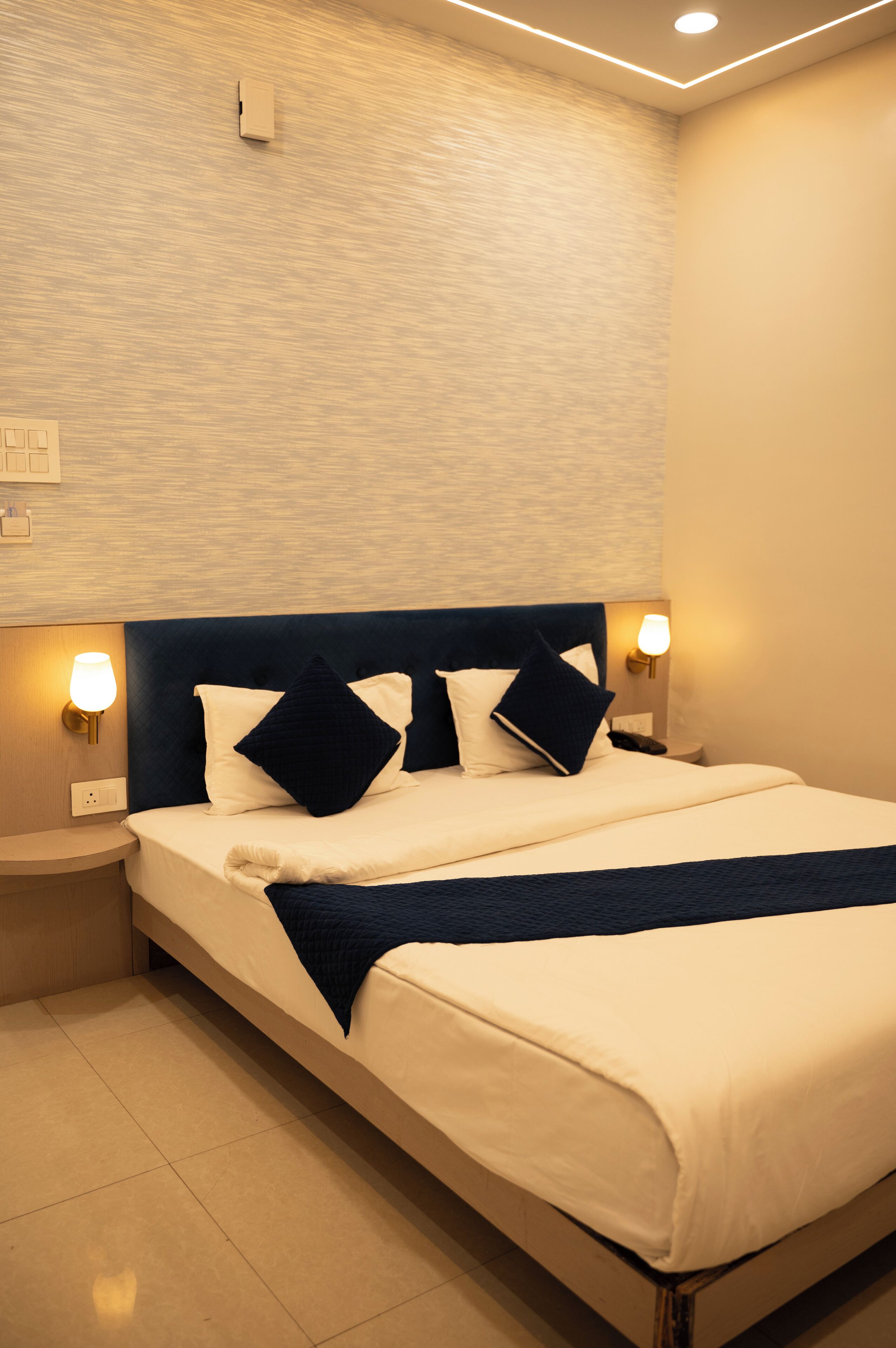 A neatly made bed with a dark headboard, two bedside lamps, and a textured wall behind.