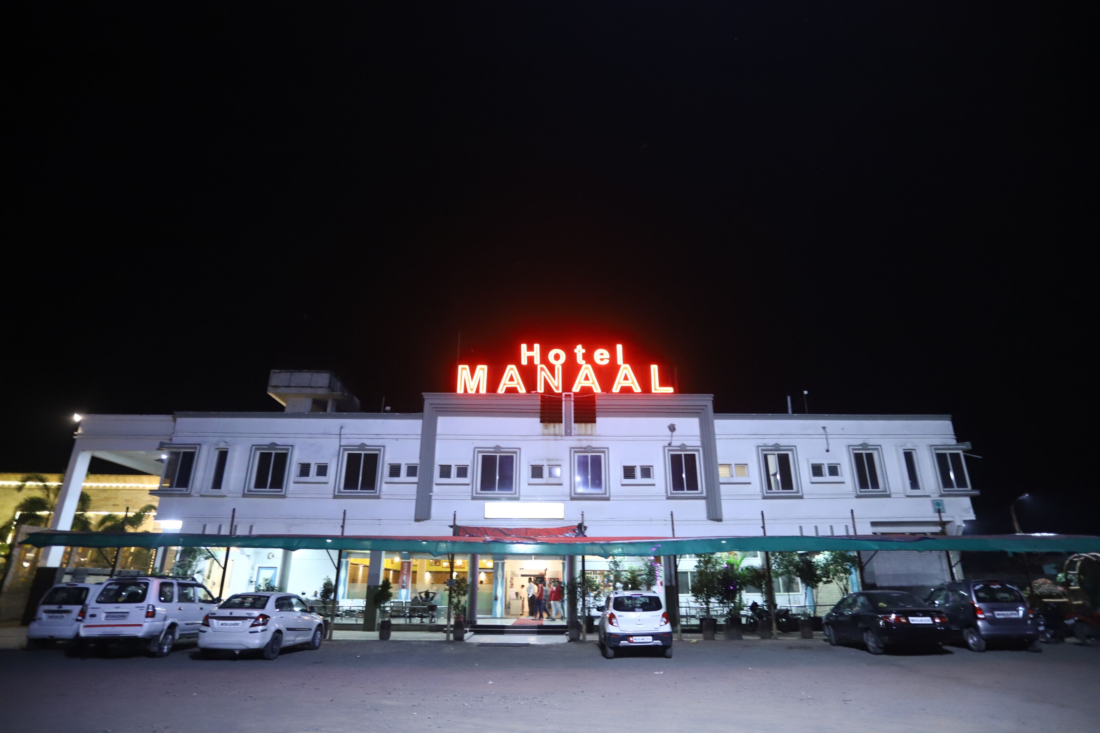 A hotel named "Hotel Maanal" with a well-lit facade and multiple cars parked in front.