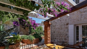 An outdoor patio with a wooden table set for two, surrounded by stone walls and potted plants. - Marijan by Interhome (Brač/Sutivan)