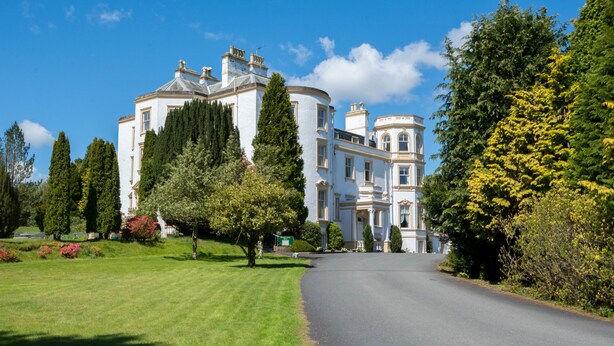 A large, white, historic building with a curved facade, surrounded by well-maintained lawns and trees. - Kirroughtree Country House B&B (Newton Stewart)