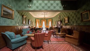 A room with green patterned wallpaper, wooden paneling, and a red patterned carpet. There are several upholstered chairs and a sofa. - Kirroughtree Country House B&B (Newton Stewart)
