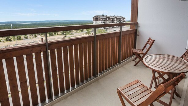 Een balkon met een houten hekwerk, een ronde tafel en twee houten stoelen.