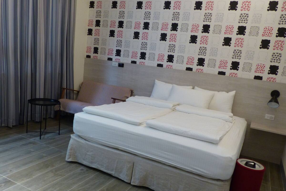 A hotel room with a bed, a chair, a small table, and a wall with a patterned design.
