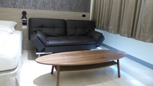Una habitación de hotel moderna con un sofá de cuero negro, una mesa de centro de madera y una cama con ropa blanca.