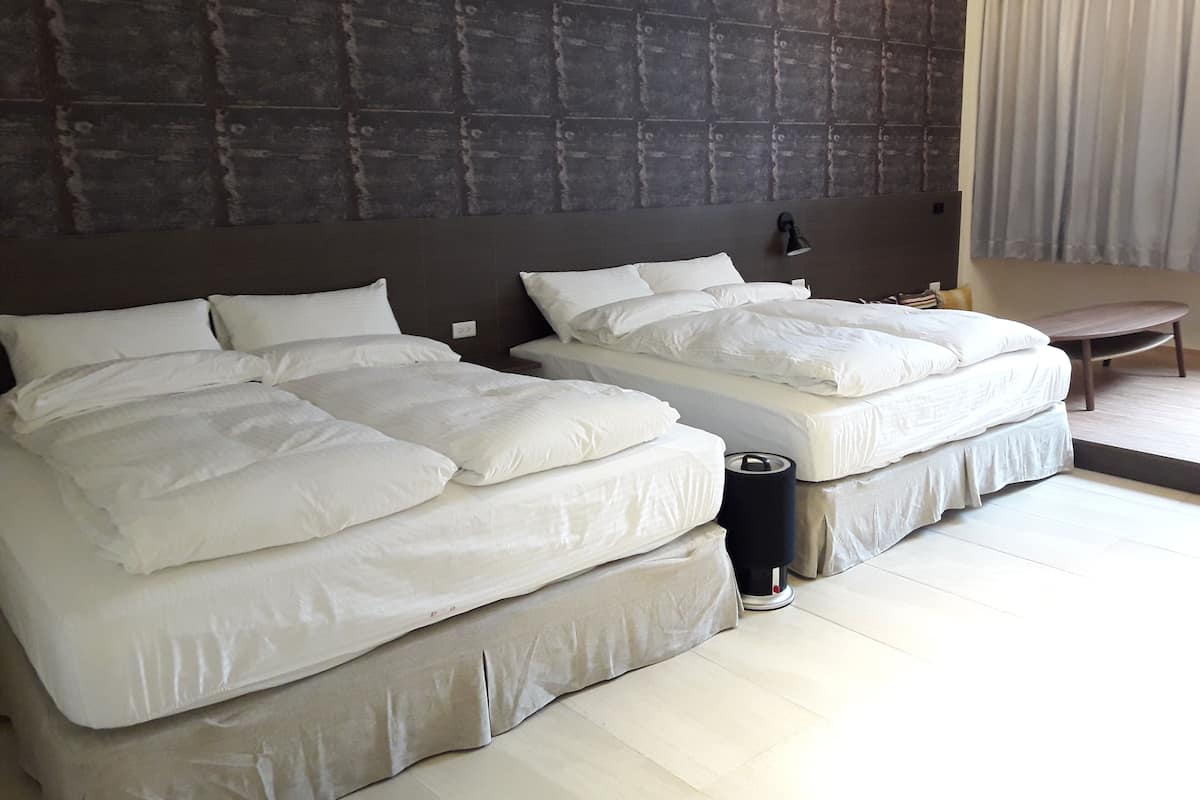 A hotel room with two beds, a dark textured wall, a bedside table, a lamp, and a chair.