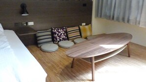 Una habitación de hotel moderna con suelo de madera, una cama, una mesita y un cabecero con lámpara.