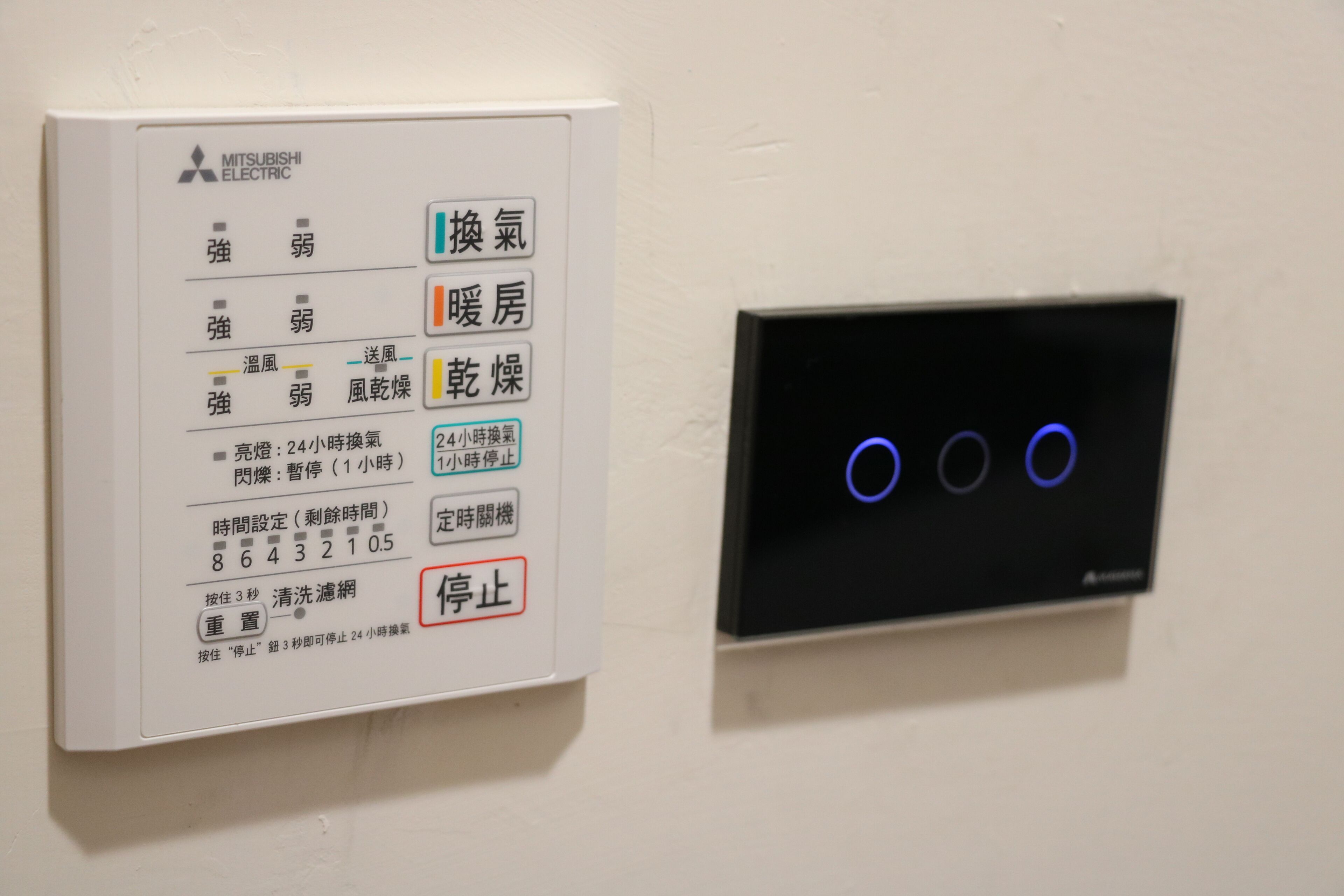 Een bedieningspaneel met Mitsubishi Electric branding, met meerdere knoppen voor functies zoals airconditioning, verwarming en ventilatorbediening.