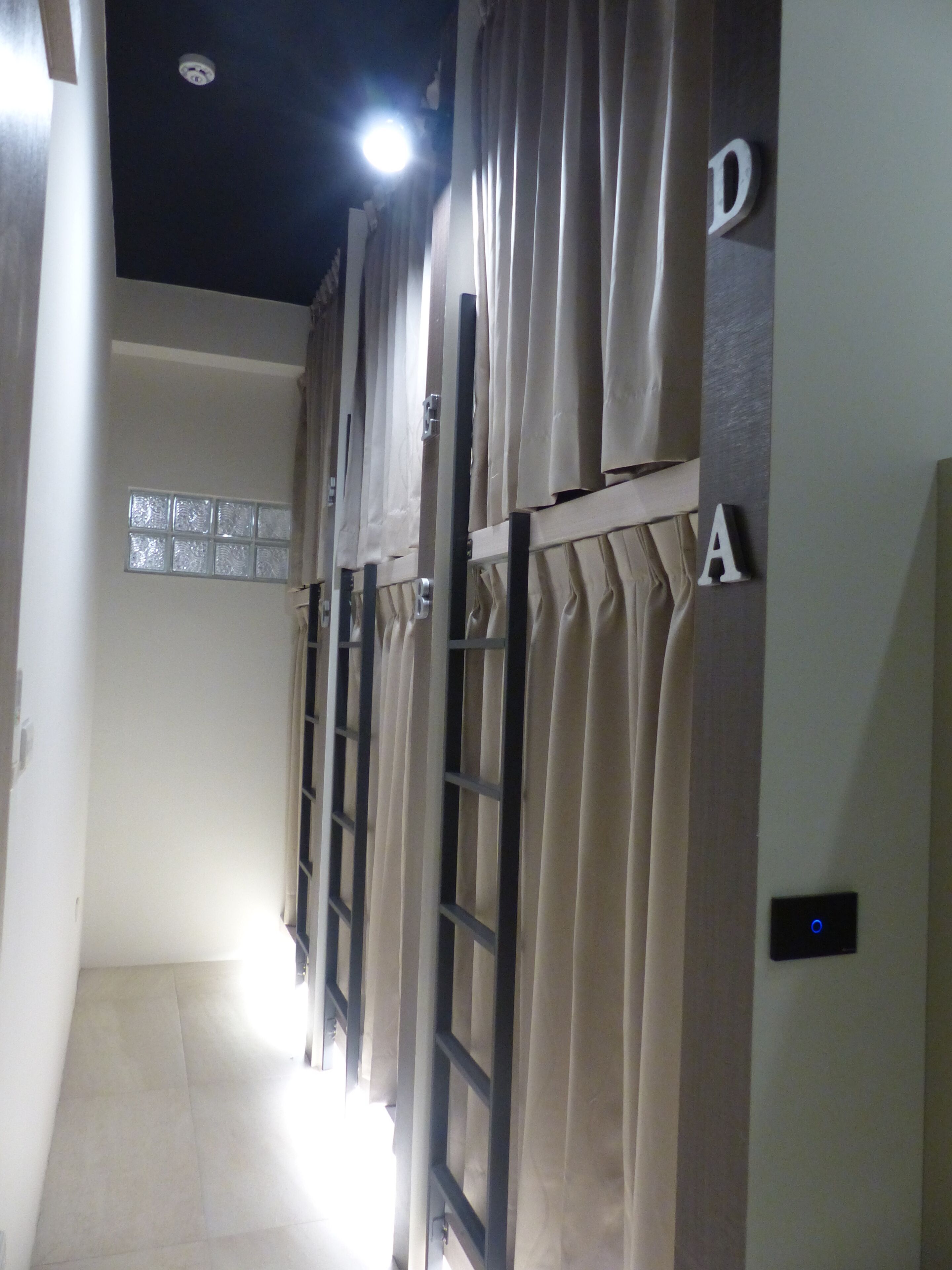 A corridor with multiple doors, each marked with a letter, leading to individual rooms.