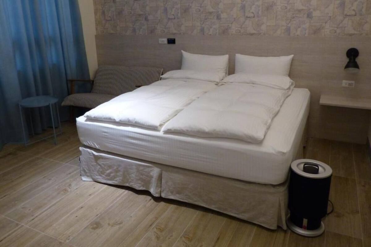 A neatly made bed with white bedding in a room with a stone-patterned wall and a blue curtain.