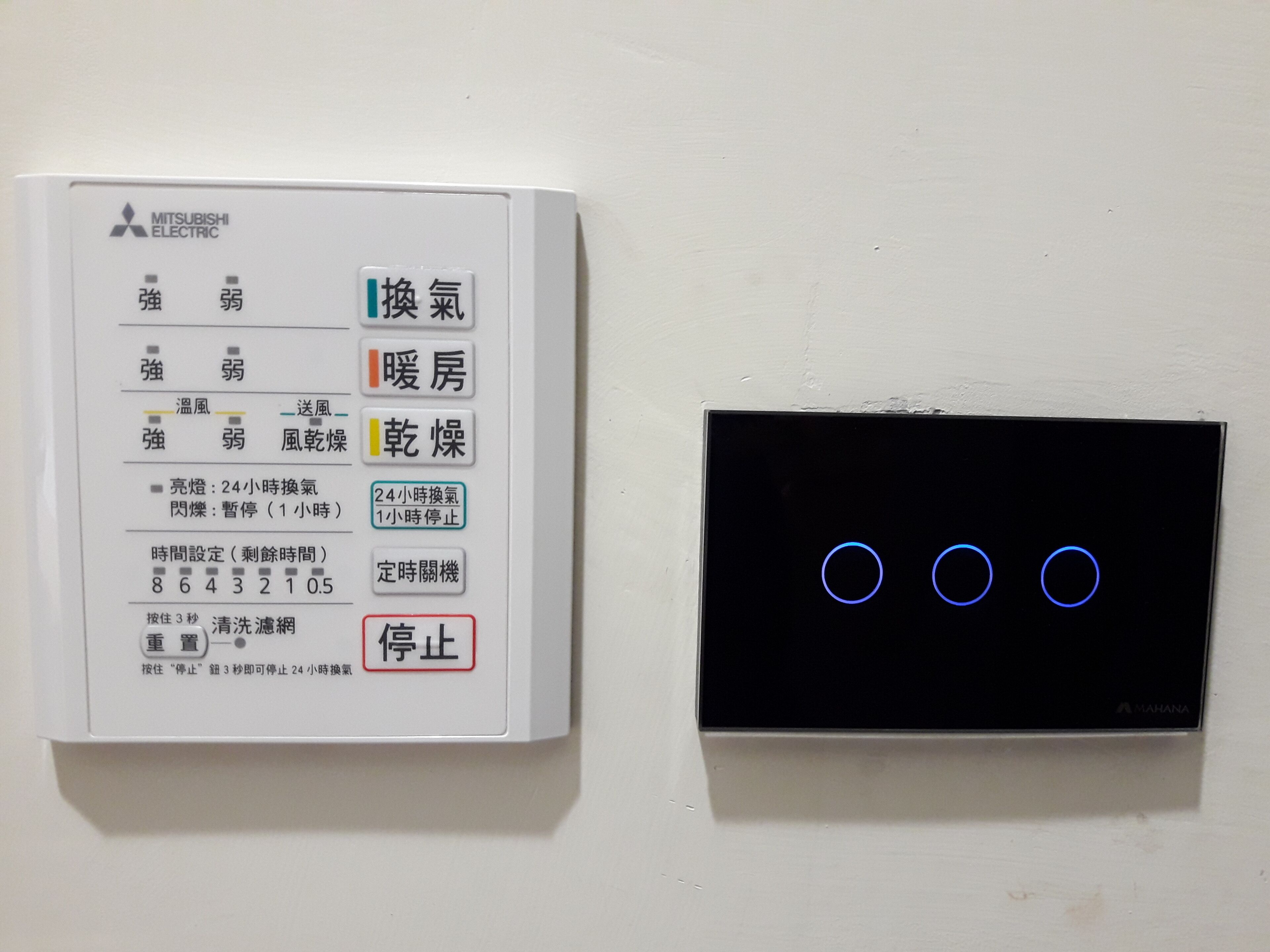 A control panel with Mitsubishi Electric branding and a black device with illuminated blue circles.