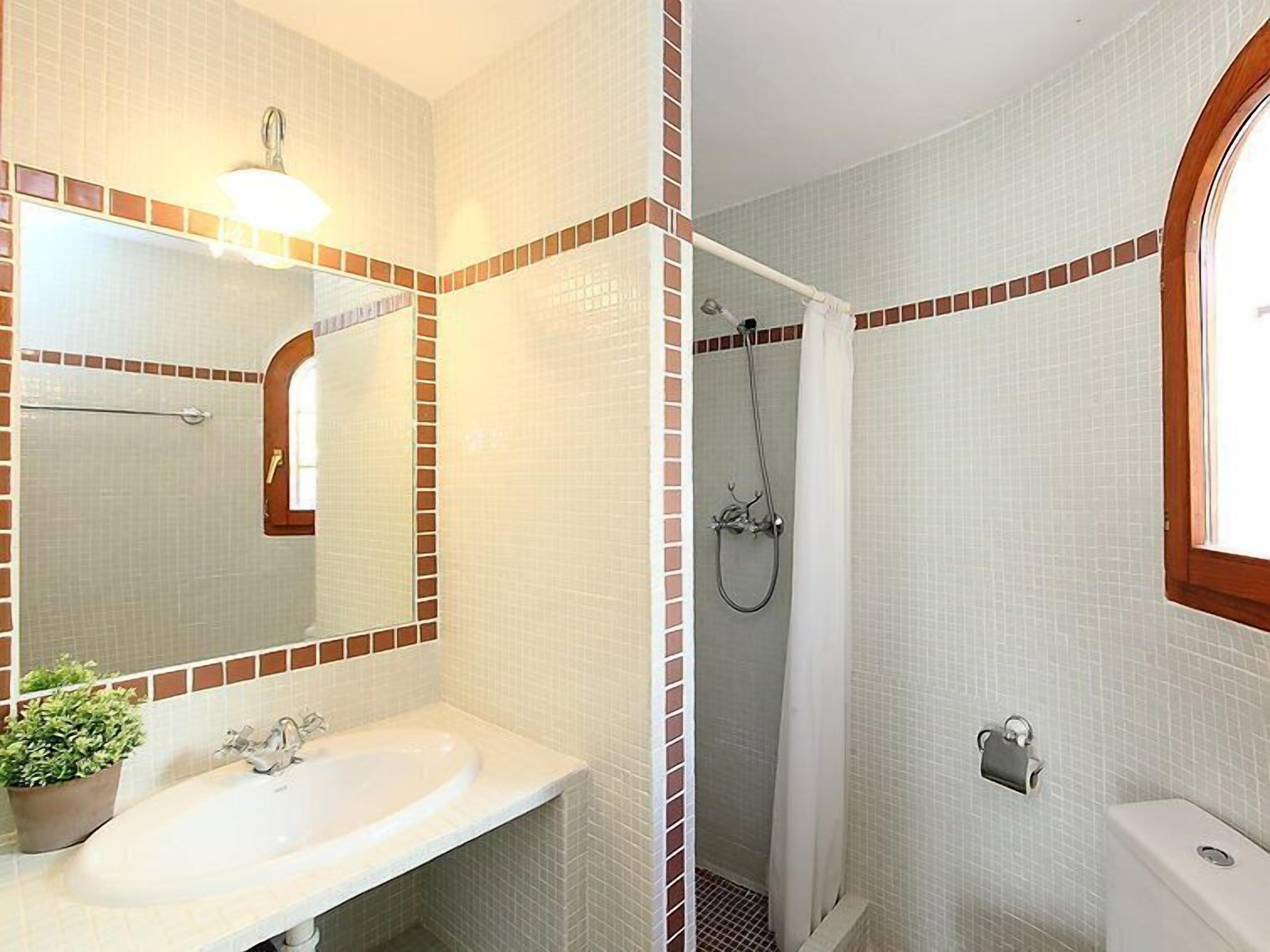 A bathroom with a white sink, a mirror, a shower with a curtain, and a toilet.