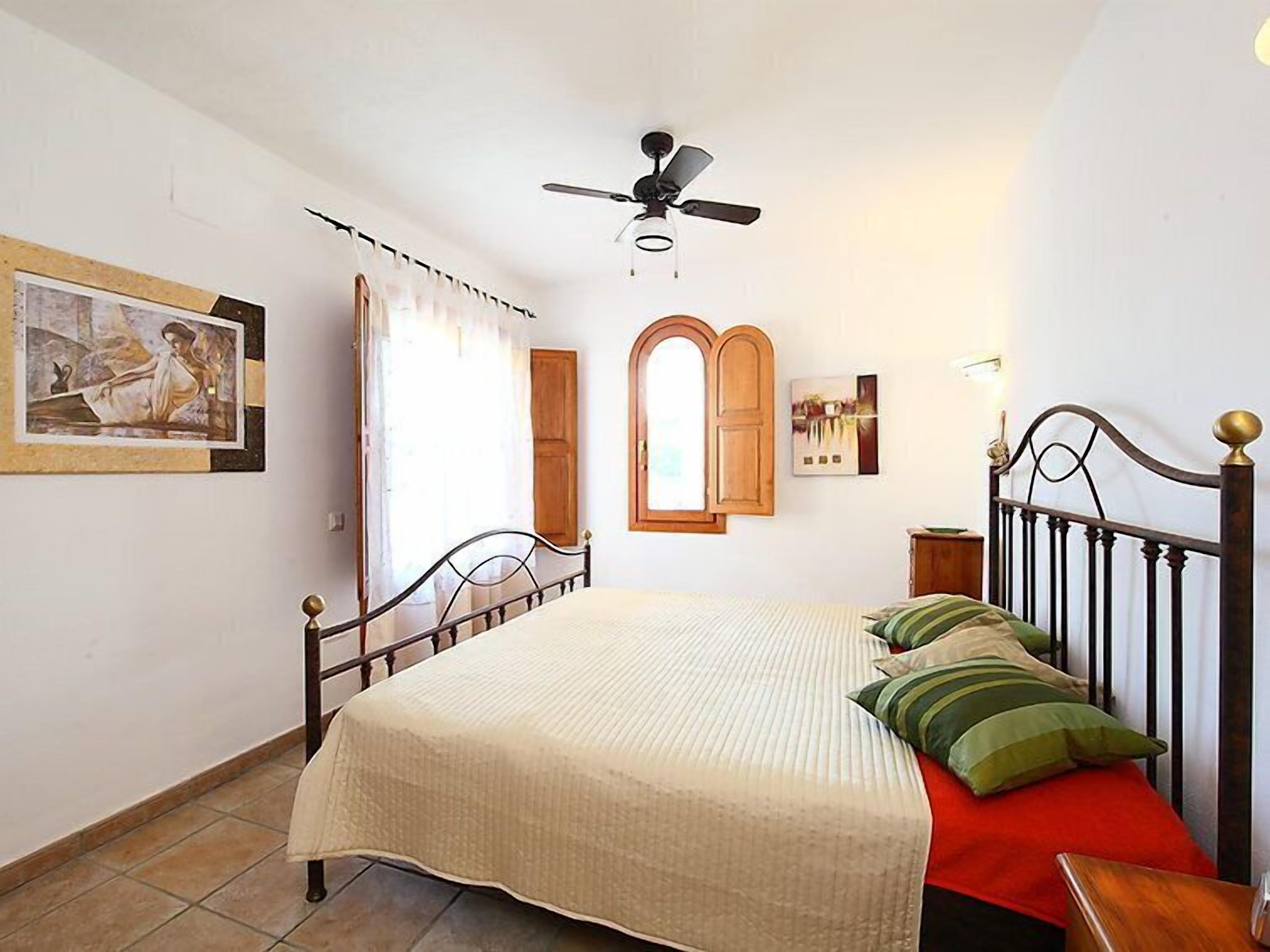 A bedroom with a bed, a ceiling fan, a window with curtains, and a wooden door.