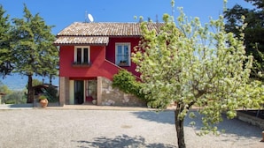 Une maison rouge avec un toit en tuiles, des fondations en pierre et une allée gravillonnée.