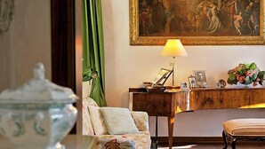Une pièce avec un canapé à motifs floraux, un bureau en bois avec une lampe, un tableau au mur et un vase rempli de fleurs.