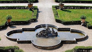 Un jardin symétrique avec une fontaine centrale, entouré de haies soigneusement taillées et de plantes en pot.