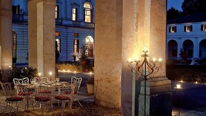 Un espace de restauration en plein air avec une table et des chaises, un chandelier et un bâtiment en arrière-plan.