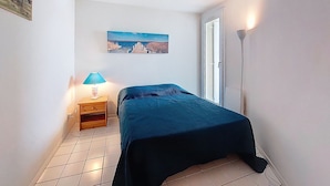 Una habitación pequeña y limpia con una cama, una mesita de noche, una lámpara y un cuadro en la pared.