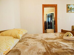 Quarto com cama, travesseiro, mesa de cabeceira e área de duche visível através de uma porta aberta.