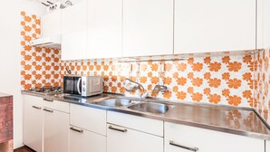 Keittiössä on valkoiset kaapit, ruostumattomasta teräksestä valmistettu työtaso ja oranssilla kukkakuviolla koristeltu välitila.