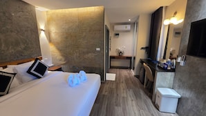Quarto de hotel com cama, mesa de cabeceira, luminária e pequena escrivaninha com cadeira.