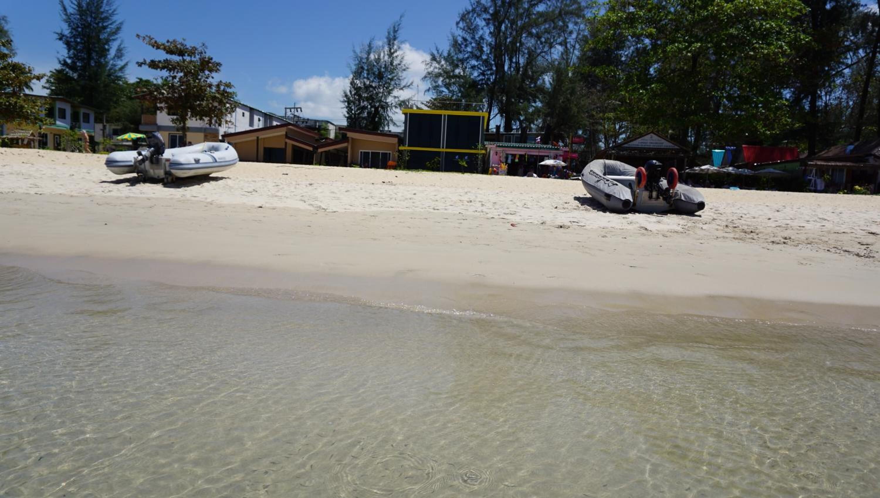 A beach with clear shallow water, a boat, and a building in the background.