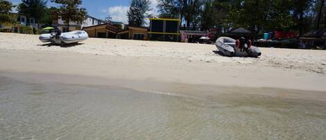 A beach with clear shallow water, a boat, and a building in the background.