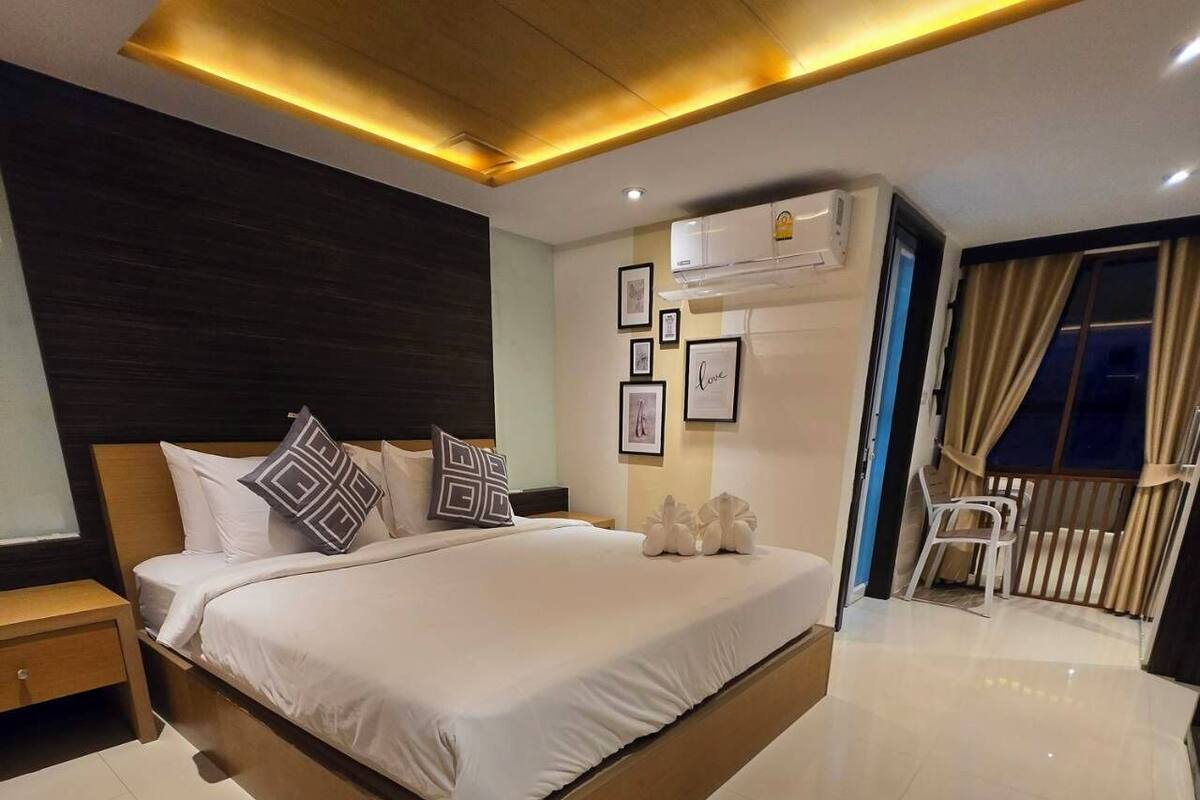 Ein modernes Hotelzimmer mit einem großen Bett, einem Nachttisch, Bildern an der Wand und einem Blick ins Freie durch ein Fenster mit Vorhängen.