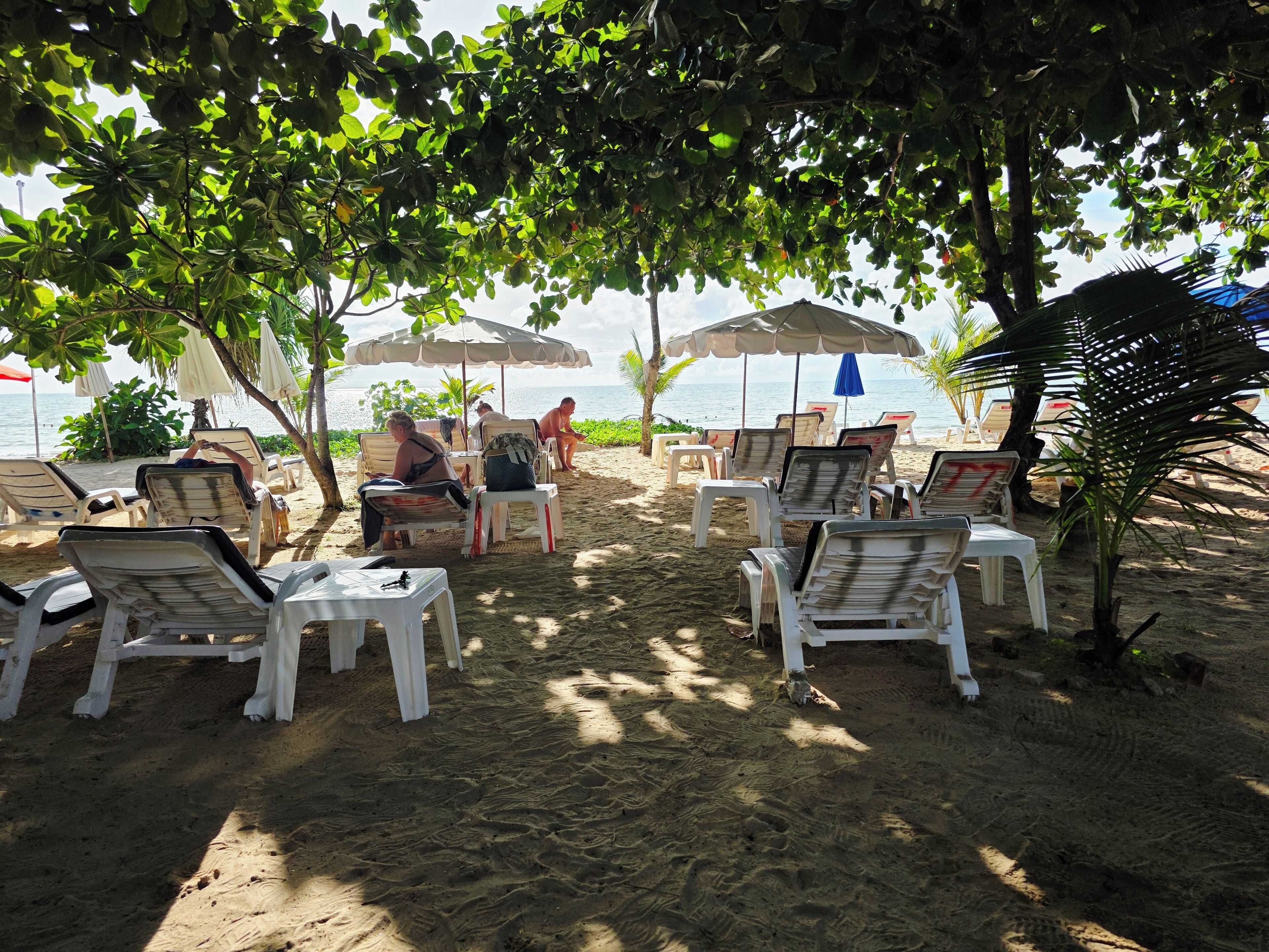 A beachside lounge with white plastic chairs and umbrellas, a sandy beach, and a view of the sea.