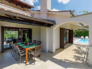 A covered outdoor dining area with a table and chairs, a pool, and a view of greenery. - Suncana by Interhome (Porec)
