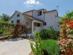 A two-story house with a tiled roof, a small porch, and a garden with various plants. - Suncana by Interhome (Porec)