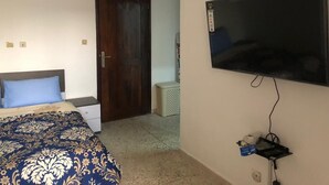 Ein Schlafzimmer mit einem Bett, einem an der Wand montierten Fernseher, einer Tür und einem kleinen weißen Nachttisch.