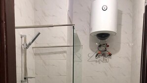 Ein Badezimmer mit Duschkabine aus Glas, Toilette und Durchlauferhitzer.