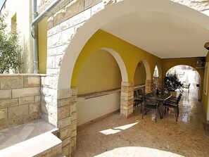 Une terrasse extérieure couverte, dotée de murs en pierre et d’arches, avec une table à manger et des chaises, ainsi qu’un sol carrelé.