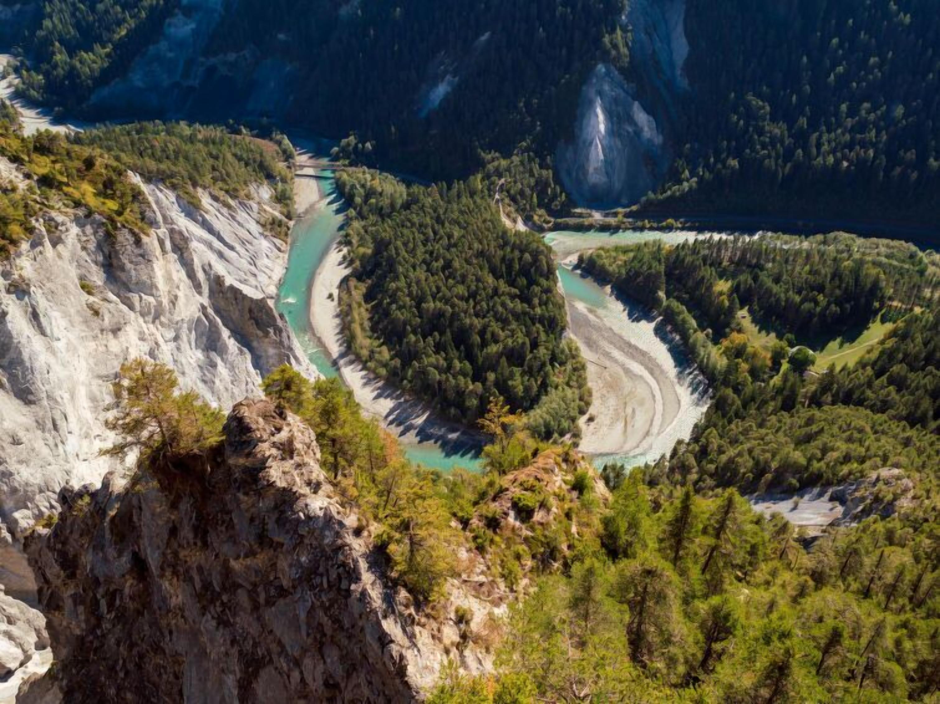 A mountainous landscape with a winding river, dense forest, and rocky cliffs.