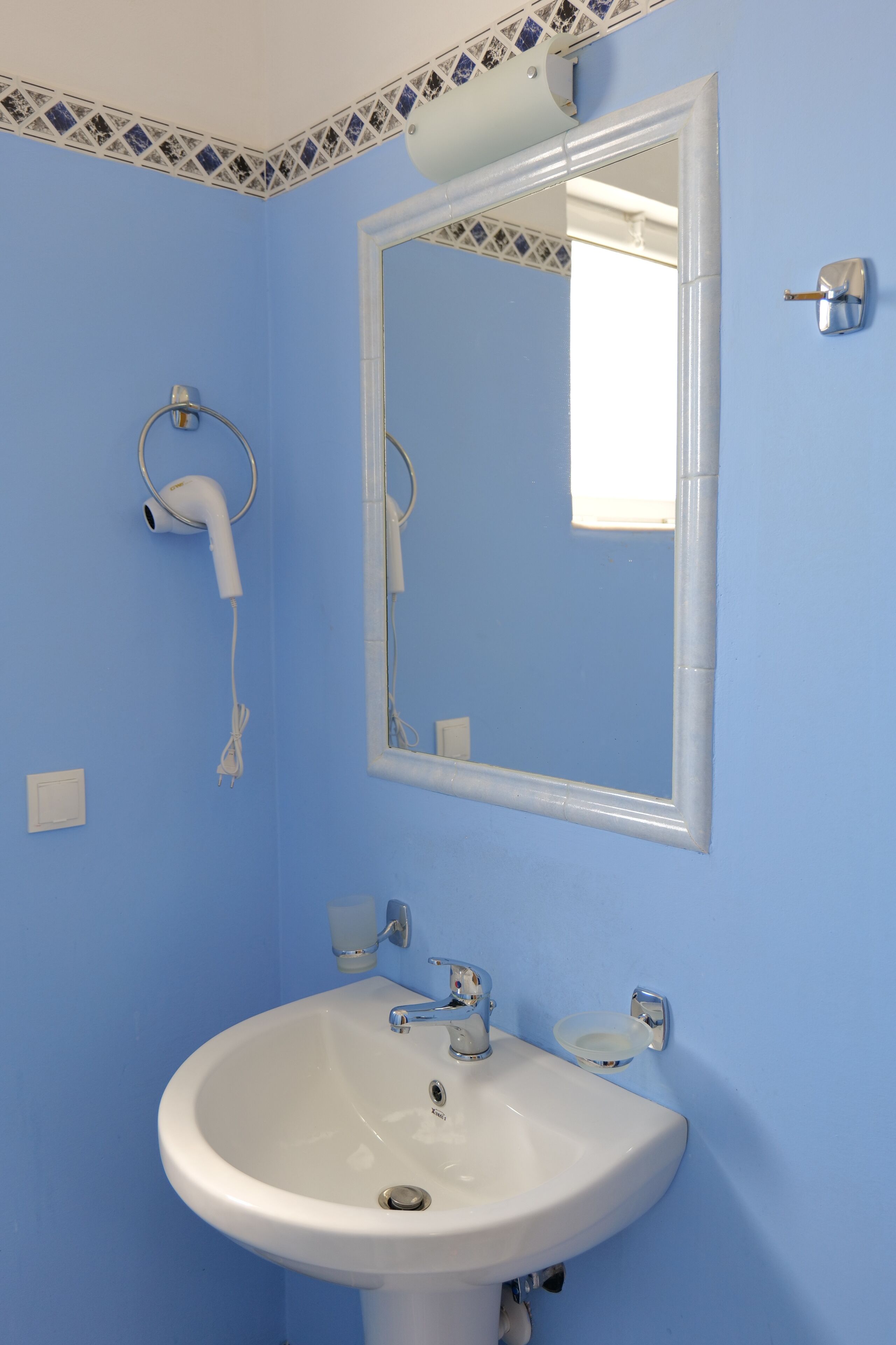 Un baño con pared azul, lavamanos blanco, espejo y secador de pelo montado en la pared.