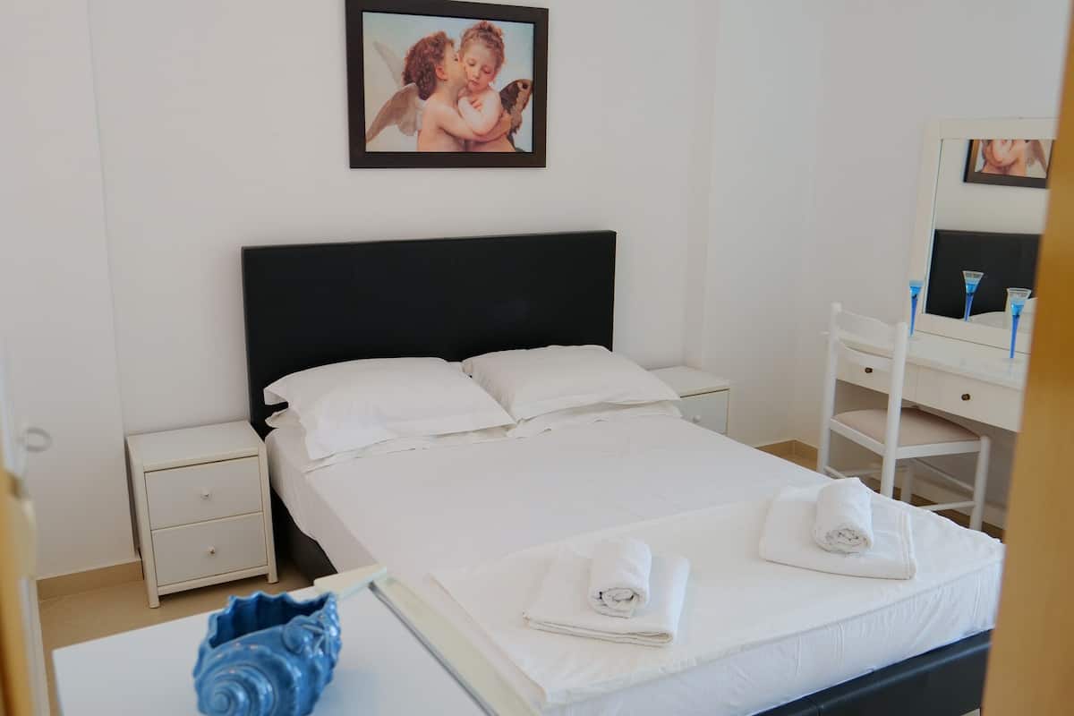 A hotel room with a bed, a nightstand, a dresser, and a small refrigerator.