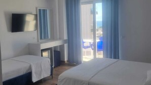 A hotel room with two beds, a TV, an air conditioning unit, a desk, and a view of the outside.