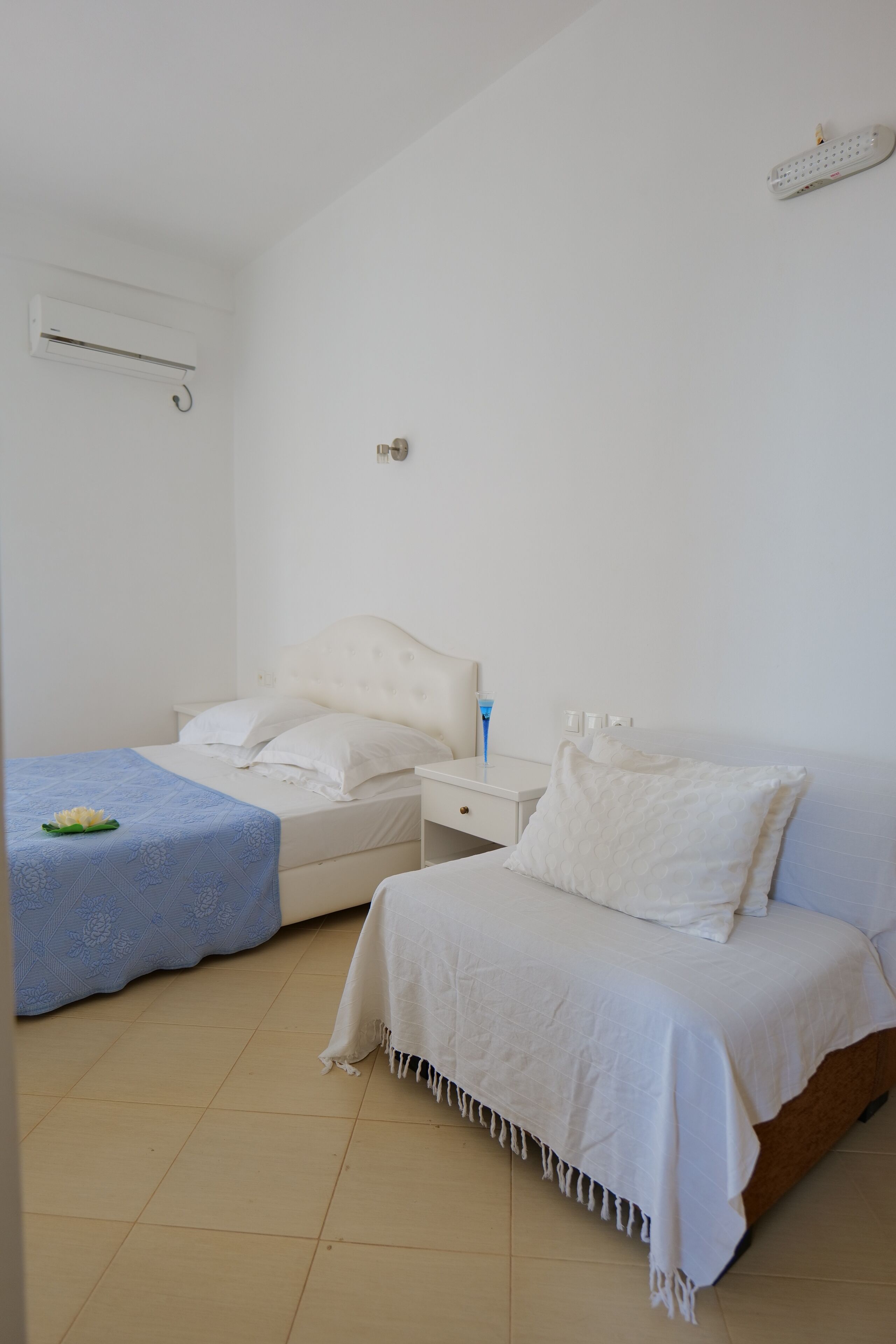 Une chambre avec deux lits, une table de chevet et une commode, ainsi qu’un climatiseur fixé au mur.