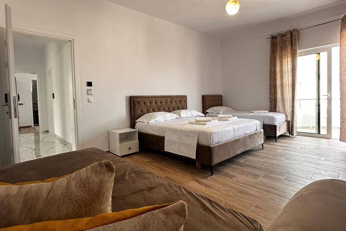 A bedroom with a large bed, two bedside tables, a wardrobe, and a door leading to another room.