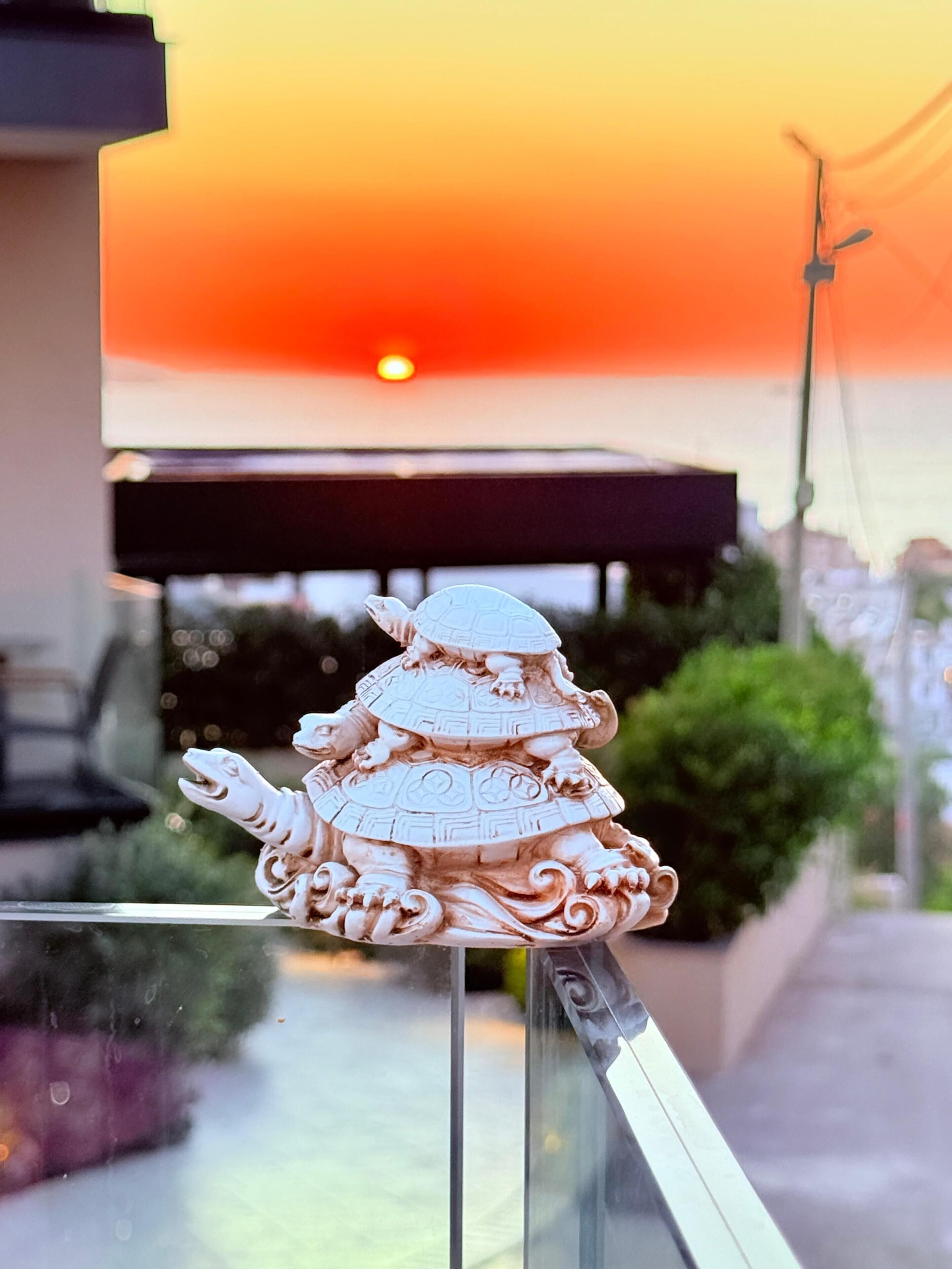 Un élément décoratif en céramique, placé sur la rambarde d’un balcon, avec un coucher de soleil en arrière-plan.